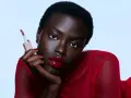 Mujer con labios rojos brillantes y un aplicador de brillo labial. Sus cejas rojas resaltan su mirada intensa.