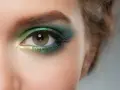 Ojo con maquillaje verde esmeralda y dorado, delineado azul y cejas verdes.