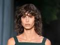Mujer con pelo rizado y flequillo despeinado, un ejemplo de los tipos de flequillo para pelo rizado que realzan la textura natural.