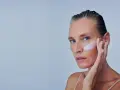 Mujer se aplica crema en la mejilla, como si fuera a quitar autobronceador. Suave toque para una piel radiante.