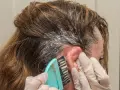 Manos enguantadas aplican tinte en el cabello. Si te manchas la piel, aprende como quitar el tinte de la piel fácilmente.