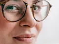 Primer plano de una mujer con gafas de montura de carey, sus ojos hundidos miran hacia un lado con una leve sonrisa.