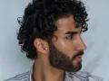 Hombre con cabello rizado y barba. Su peinado luce como si se preguntara cuanto dura una permanente rizada hombre.