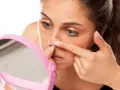 Mujer examinando diferentes tipos de granos en la nariz frente a un espejo rosa.