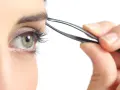 Ojo verde con pestaña larga, depilándose la ceja con pinzas. Decide cada cuanto depilarse las cejas para un look perfecto.