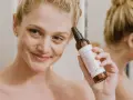 Mujer sonriente aplica bruma facial para como fijar el maquillaje. El producto es de la marca KÁLOS.