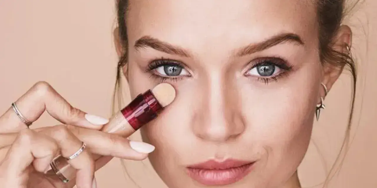 Mujer aplicando corrector para maquillar bolsas ojos. Suave aplicador y piel radiante.
