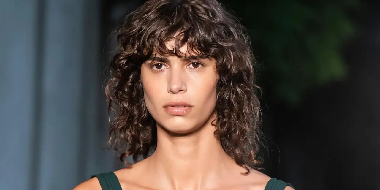 Mujer con pelo rizado y flequillo despeinado, un ejemplo de los tipos de flequillo para pelo rizado que realzan la textura natural.