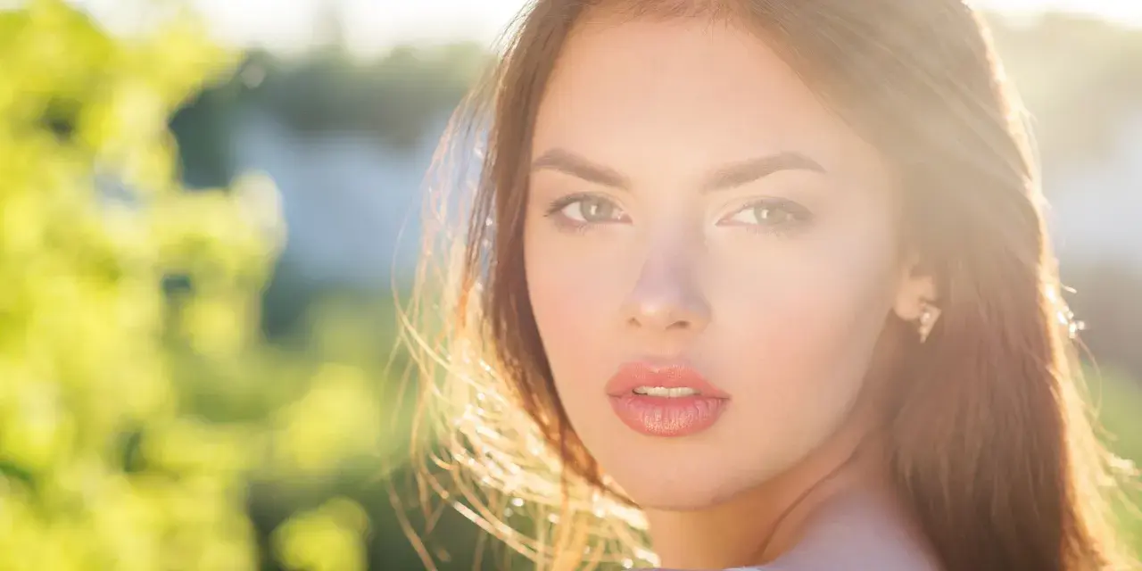 Rostro de mujer con cabello castaño y ojos verdes, iluminado por el sol. Su expresión transmite un glow up, un renacer radiante.