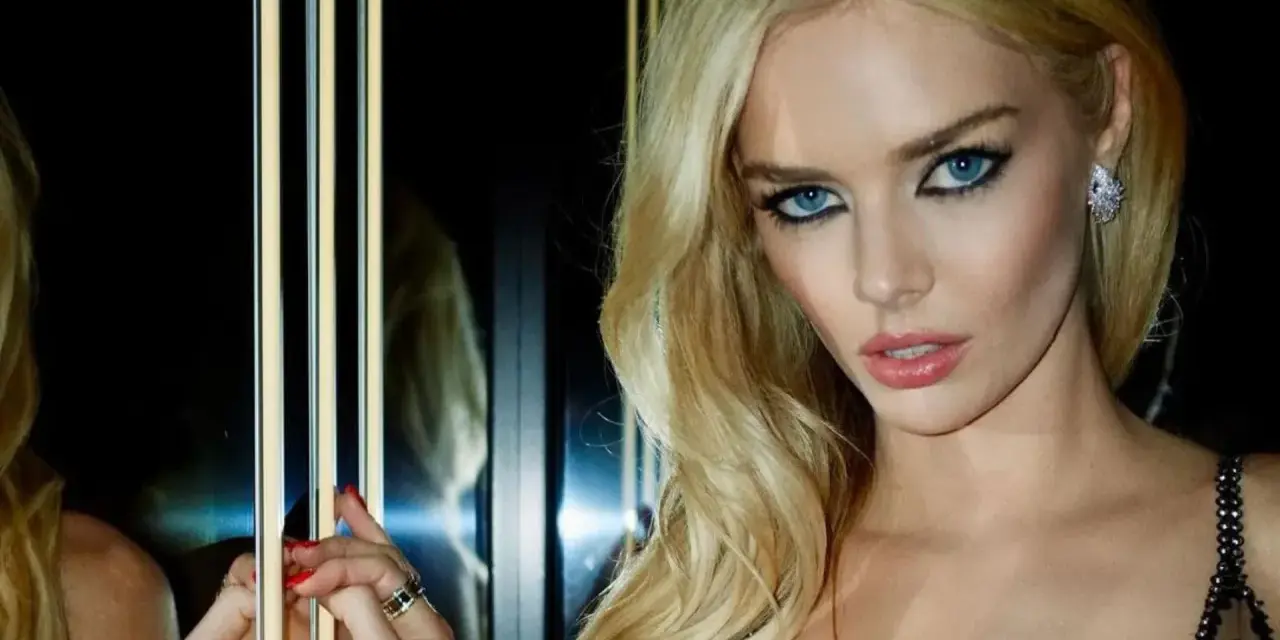 Maquillaje ojos verdes boda: rubia con ojos azules intensos, labios rosados y vestido negro brillante.