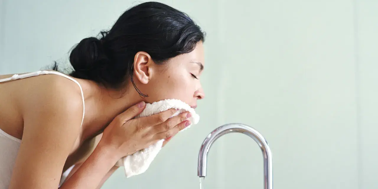 Mujer se limpia el rostro con una toalla suave, como si el agua micelar se enjuaga.