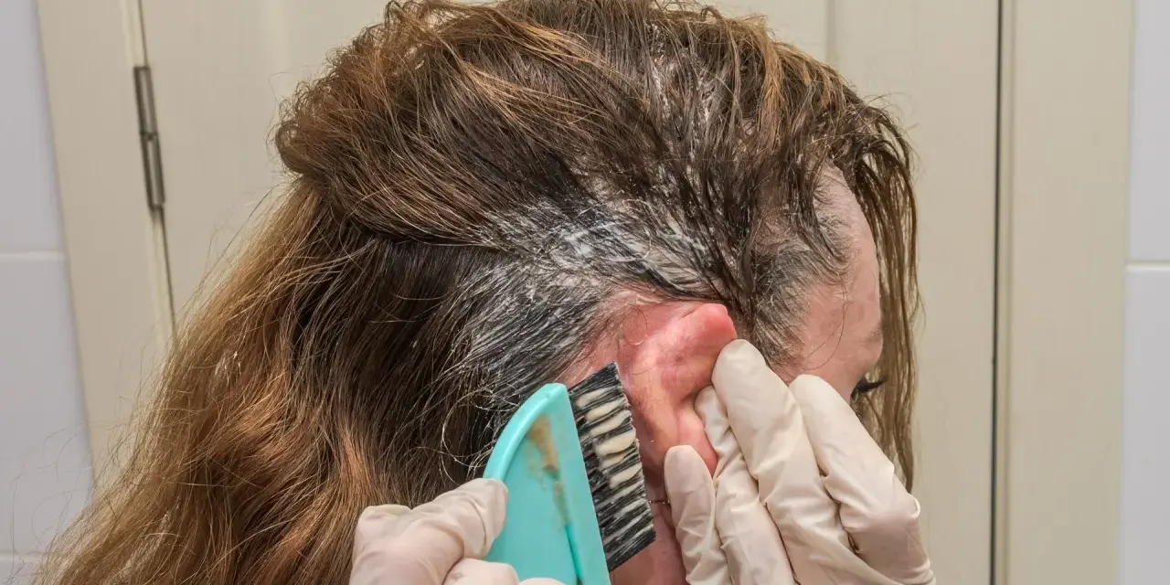 Manos enguantadas aplican tinte en el cabello. Si te manchas la piel, aprende como quitar el tinte de la piel fácilmente.