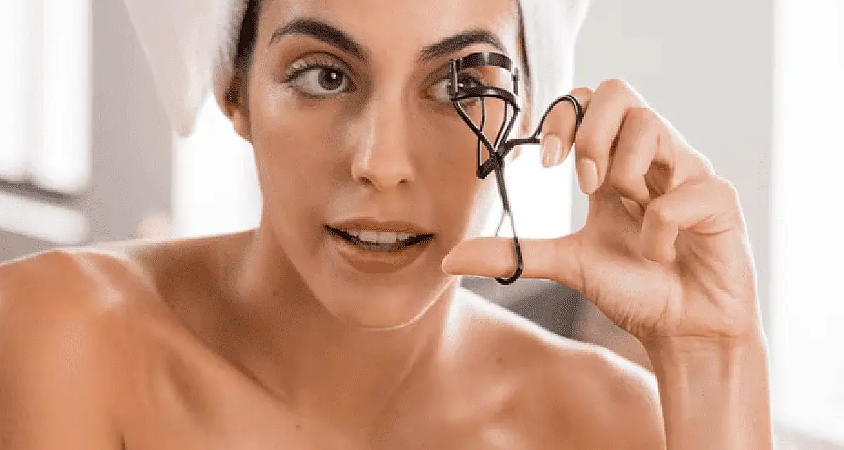 Mujer con toalla en la cabeza usa un rizador de pestañas. A veces, el rizador de pestañas es malo para tus ojos.