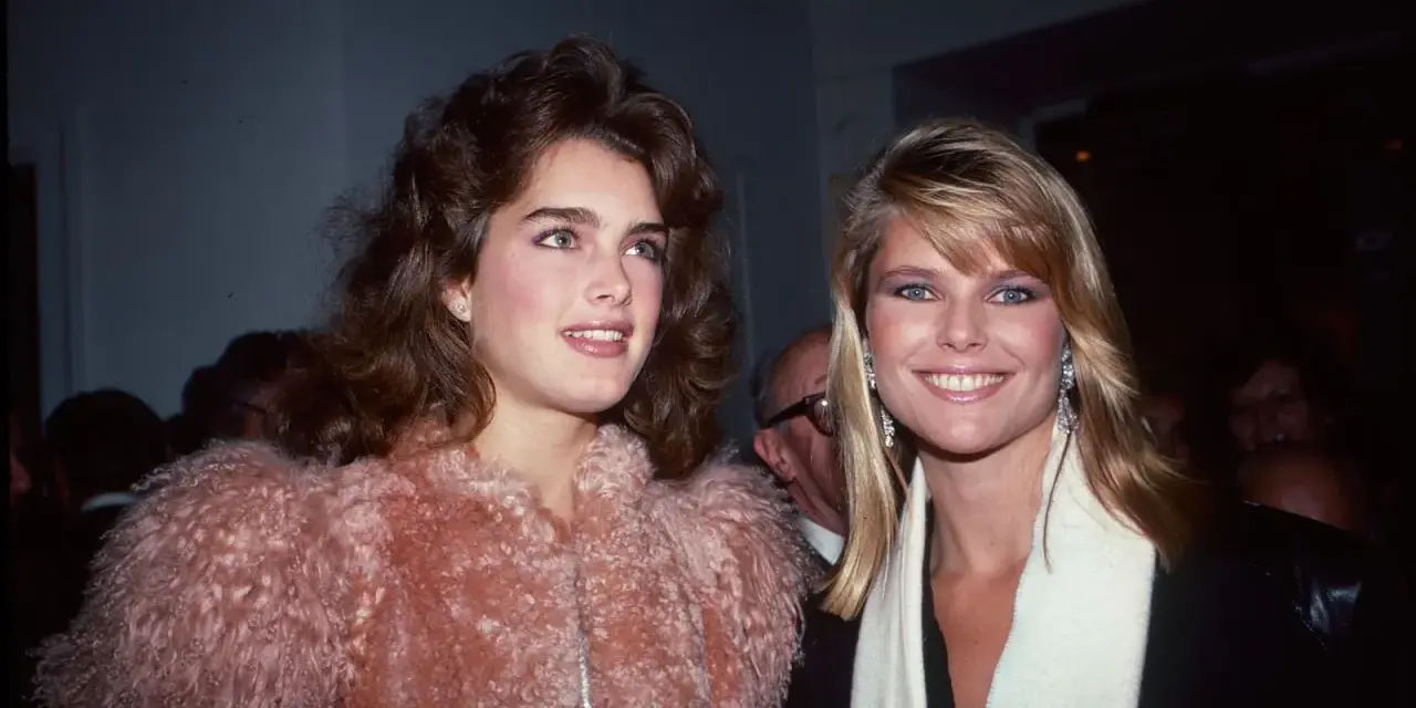 Dos mujeres con peinados icónicos de los 80, una con cabello castaño voluminoso y otra con rubio liso, posan sonrientes.