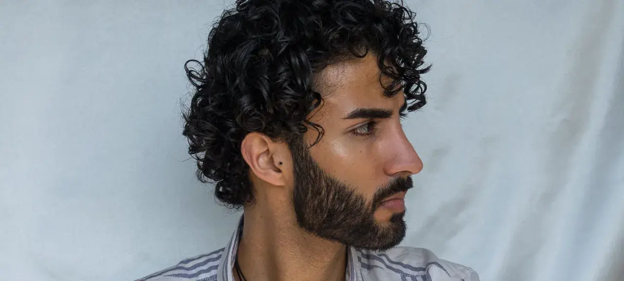 Hombre con cabello rizado y barba. Su peinado luce como si se preguntara cuanto dura una permanente rizada hombre.