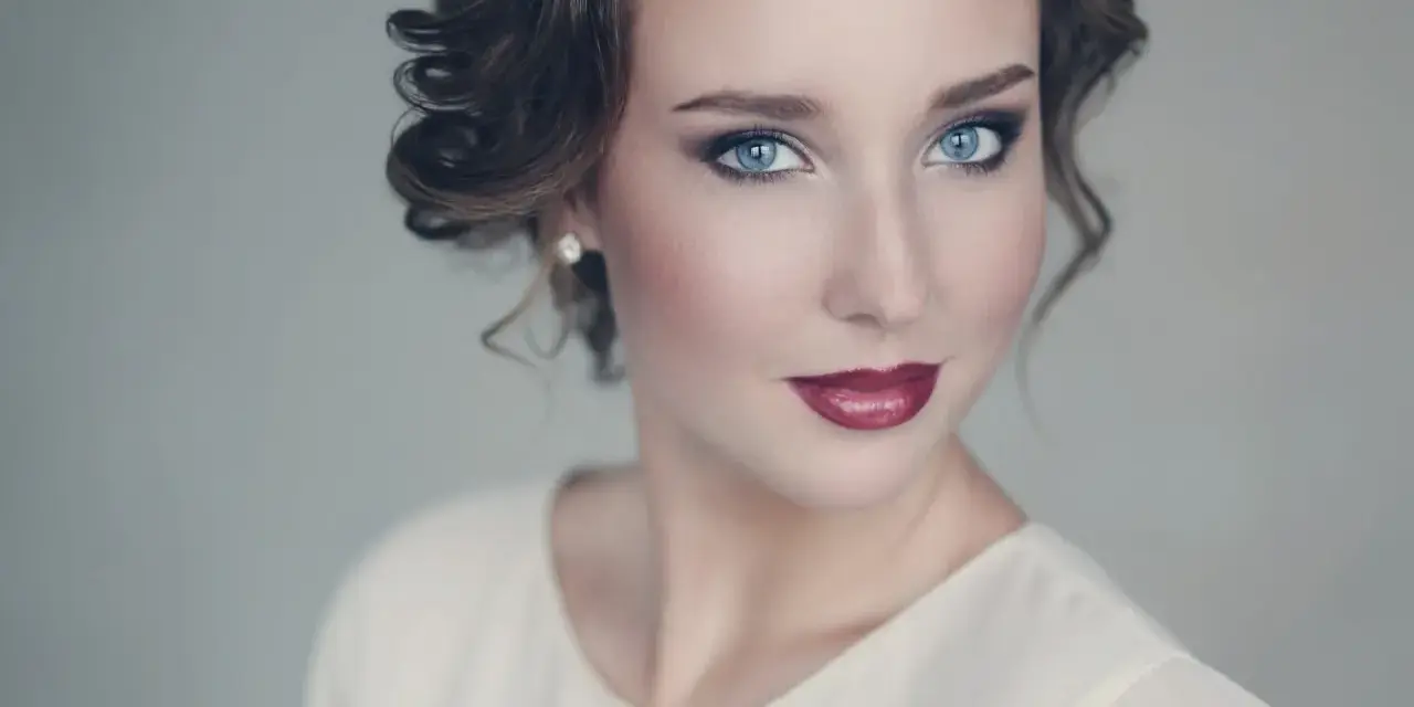 Maquillaje para vestido blanco: ojos ahumados y labios rojos intensos, peinado recogido con rizos.