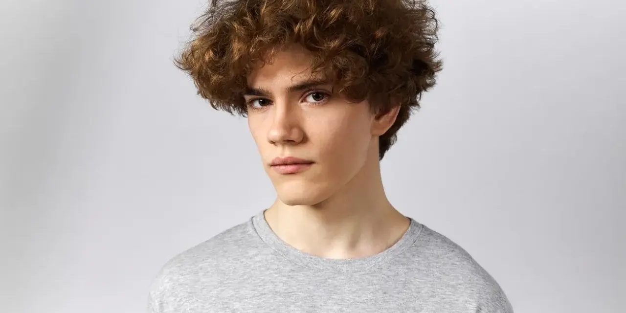 Joven con un moderno corte de pelo rizado hombre, luciendo un estilo desenfadado y juvenil.