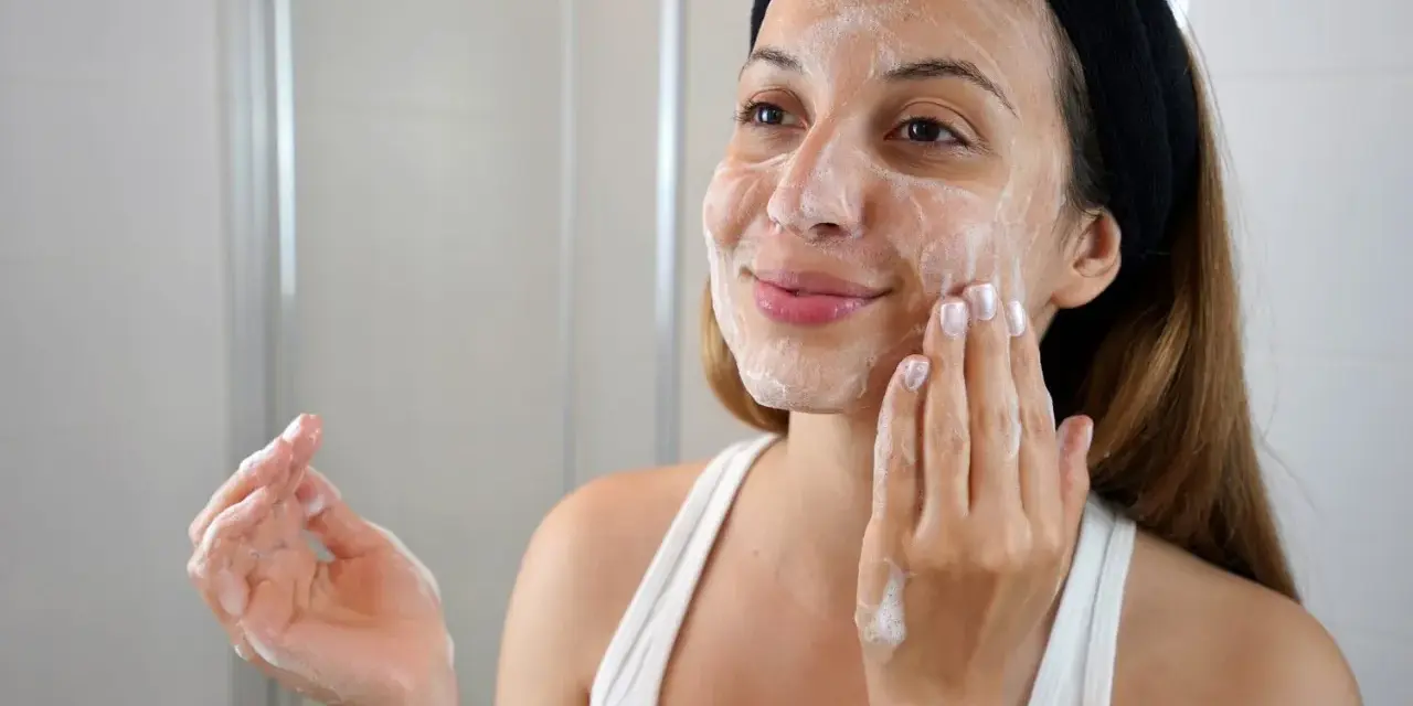 Mujer con diadema negra aplicándose espuma en el rostro, parte de su rutina de limpieza facial.