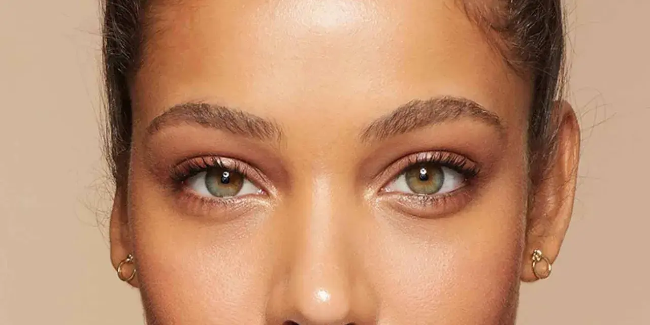 Primer plano de unos ojos verdes y marrones, mostrando cómo cambiar la forma de las cejas con maquillaje.
