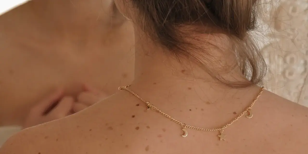 Espalda con lunares y un collar dorado con estrellas y lunas. Me pregunto porque me salen granos en la espalda.
