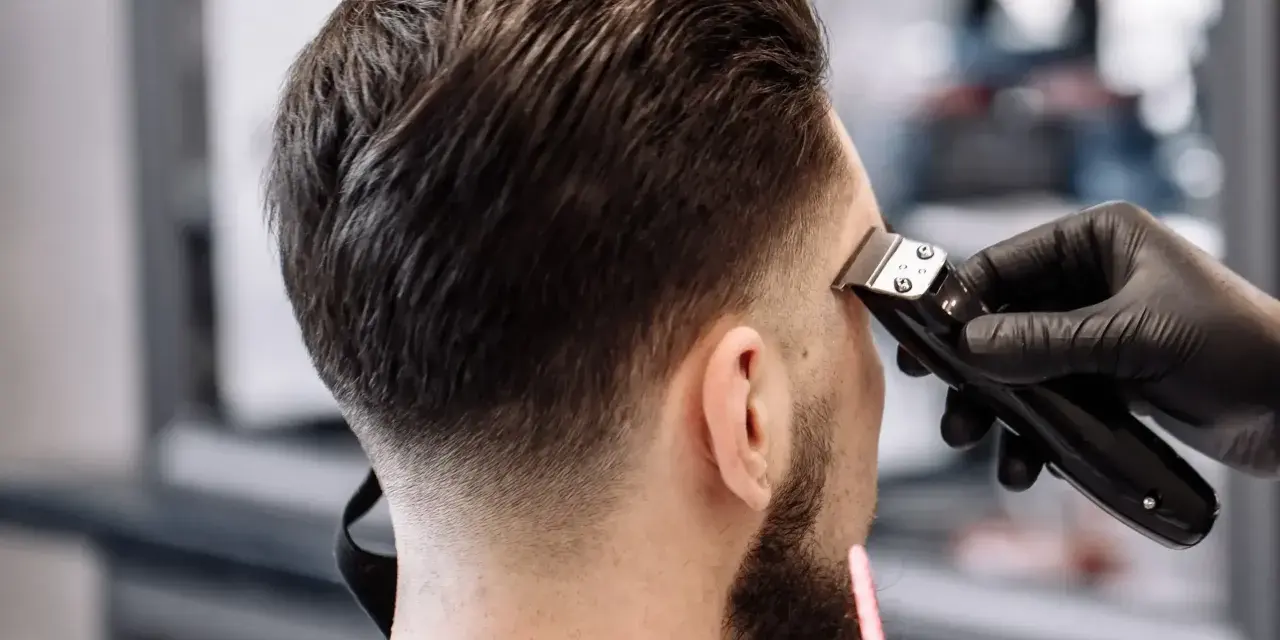 Barbero creando un tuper fade impecable en la nuca de un cliente.