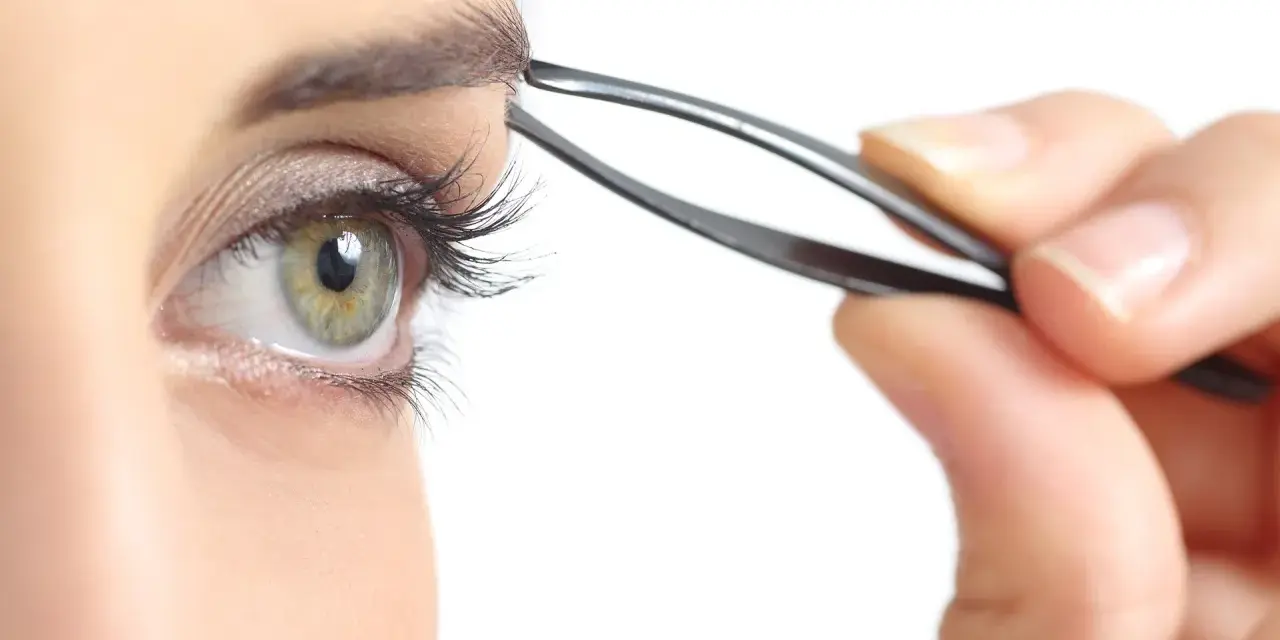 Ojo verde con pestaña larga, depilándose la ceja con pinzas. Decide cada cuanto depilarse las cejas para un look perfecto.