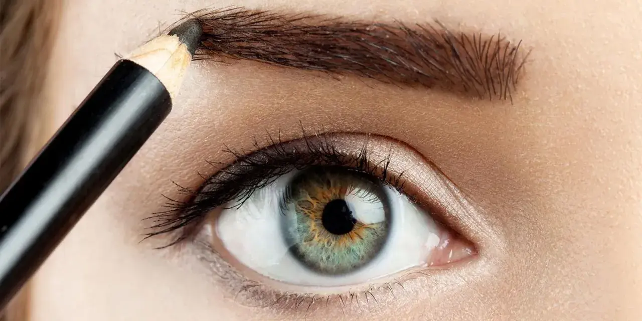 Detalle de ojo y ceja siendo maquillada con lápiz para disimular calvas.