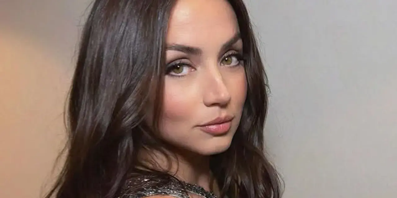 Mujer con cortes de pelo ondulado castaño, mirada intensa y vestido brillante.