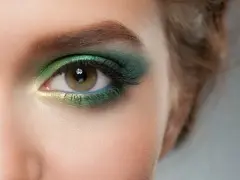 Ojo con maquillaje verde esmeralda y dorado, delineado azul y cejas verdes.
