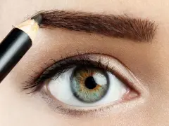 Detalle de ojo y ceja siendo maquillada con lápiz para disimular calvas.