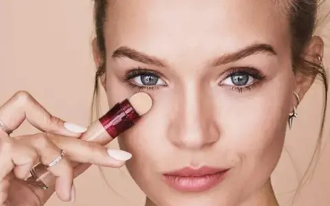 Mujer aplicando corrector para maquillar bolsas ojos. Suave aplicador y piel radiante.
