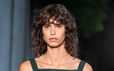 Mujer con pelo rizado y flequillo despeinado, un ejemplo de los tipos de flequillo para pelo rizado que realzan la textura natural.