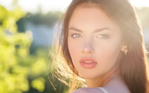 Rostro de mujer con cabello castaño y ojos verdes, iluminado por el sol. Su expresión transmite un glow up, un renacer radiante.