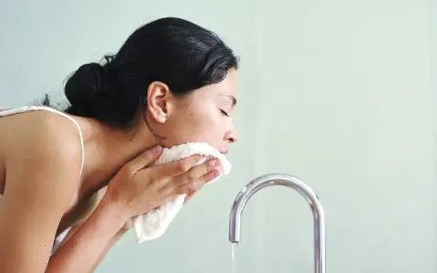 Mujer se limpia el rostro con una toalla suave, como si el agua micelar se enjuaga.