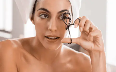 Mujer con toalla en la cabeza usa un rizador de pestañas. A veces, el rizador de pestañas es malo para tus ojos.