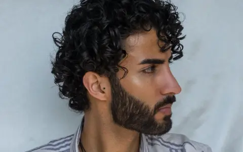 Hombre con cabello rizado y barba. Su peinado luce como si se preguntara cuanto dura una permanente rizada hombre.