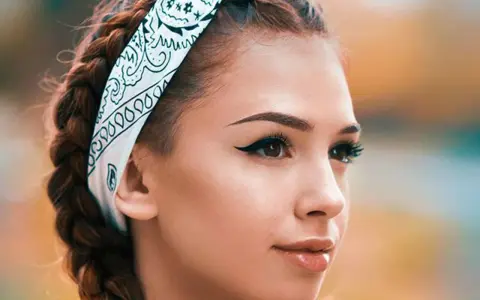Chica con trenzas y pañuelo, mostrando cómo pintar la raya del ojo con delineado cat eye perfecto.