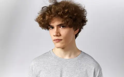 Joven con un moderno corte de pelo rizado hombre, luciendo un estilo desenfadado y juvenil.