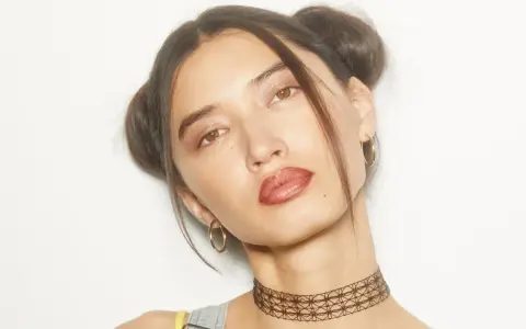 Chica con peinados y maquillaje de los 90, dos moños altos, labios marrones y choker.