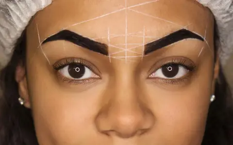 Ojos y cejas marcadas con líneas blancas para diseño. Se observa una posible alergia a la henna en las cejas.