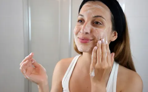 Mujer con diadema negra aplicándose espuma en el rostro, parte de su rutina de limpieza facial.