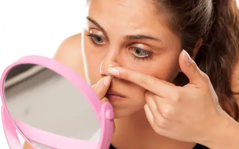 Mujer examinando diferentes tipos de granos en la nariz frente a un espejo rosa.