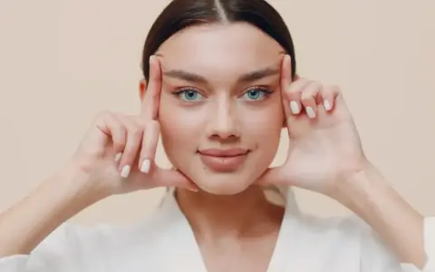 Mujer con ojos azules realizando ejercicios faciales, aplicando presión en las sienes y barbilla para tonificar.