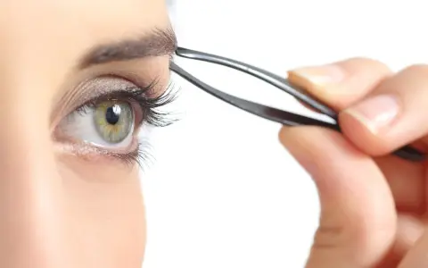 Ojo verde con pestaña larga, depilándose la ceja con pinzas. Decide cada cuanto depilarse las cejas para un look perfecto.