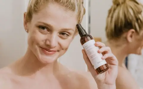 Mujer sonriente aplica bruma facial para como fijar el maquillaje. El producto es de la marca KÁLOS.