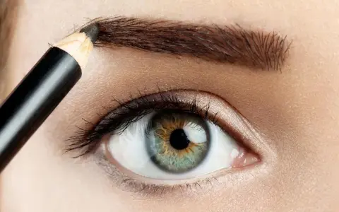 Detalle de ojo y ceja siendo maquillada con lápiz para disimular calvas.