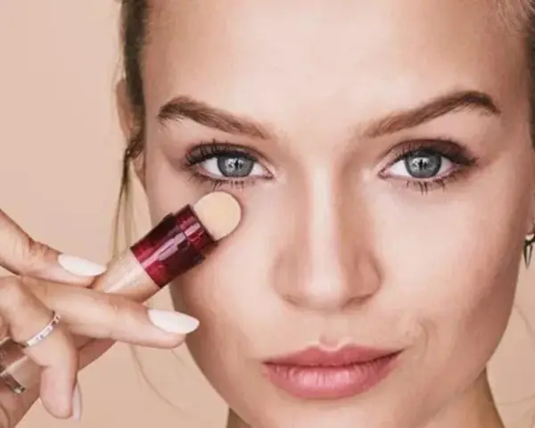 Mujer aplicando corrector para maquillar bolsas ojos. Suave aplicador y piel radiante.