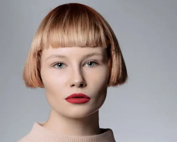 Mujer con pelo corto con flequillo desfilado, ojos azules y labios rojos.
