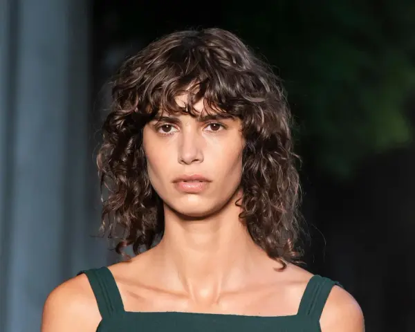 Mujer con pelo rizado y flequillo despeinado, un ejemplo de los tipos de flequillo para pelo rizado que realzan la textura natural.