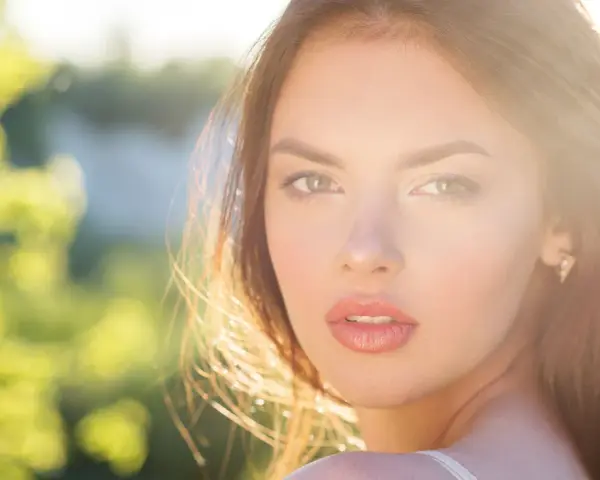 Rostro de mujer con cabello castaño y ojos verdes, iluminado por el sol. Su expresión transmite un glow up, un renacer radiante.